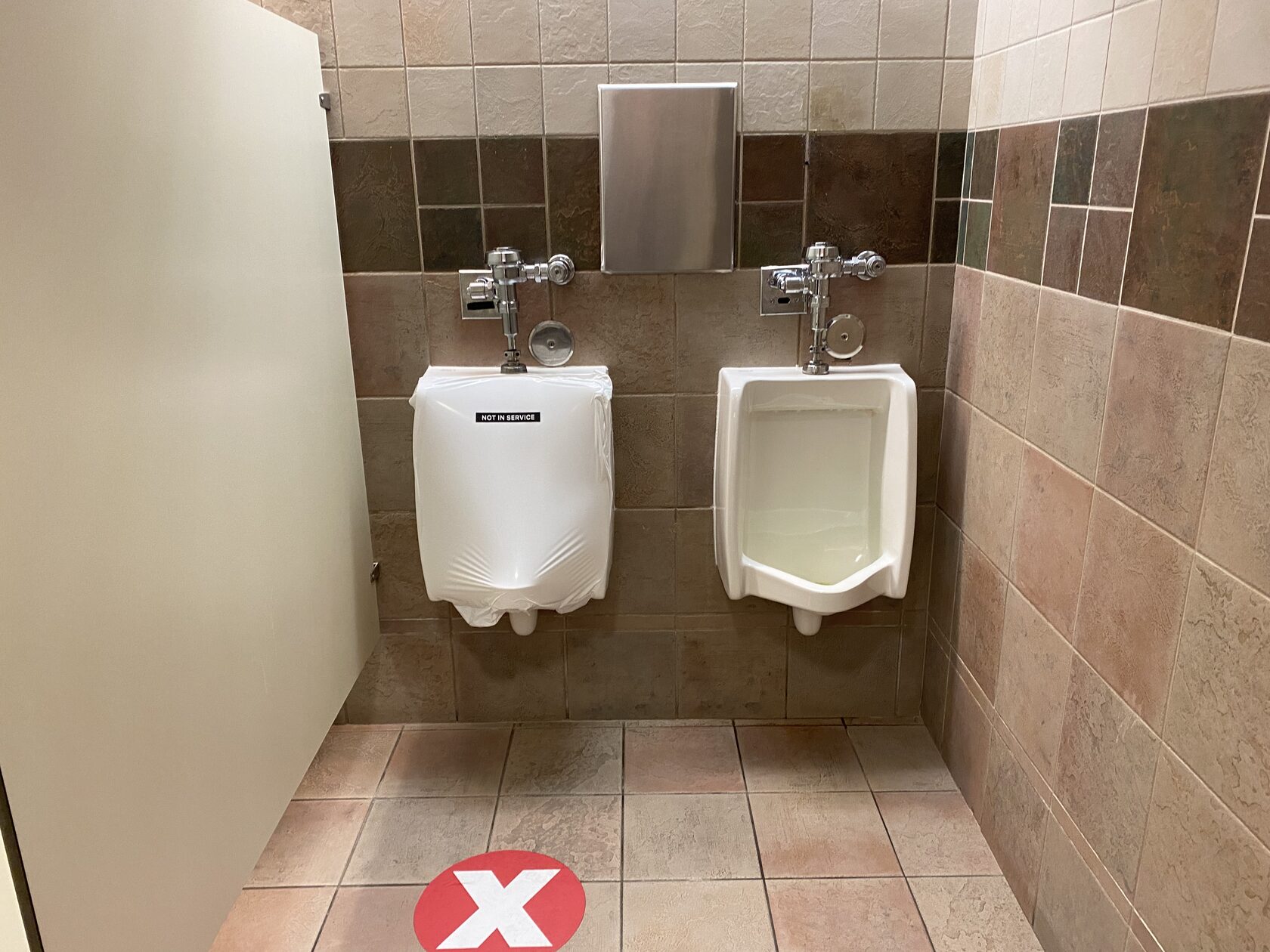 Commercial restroom with one urinal neatly covered and labelled Not in Service